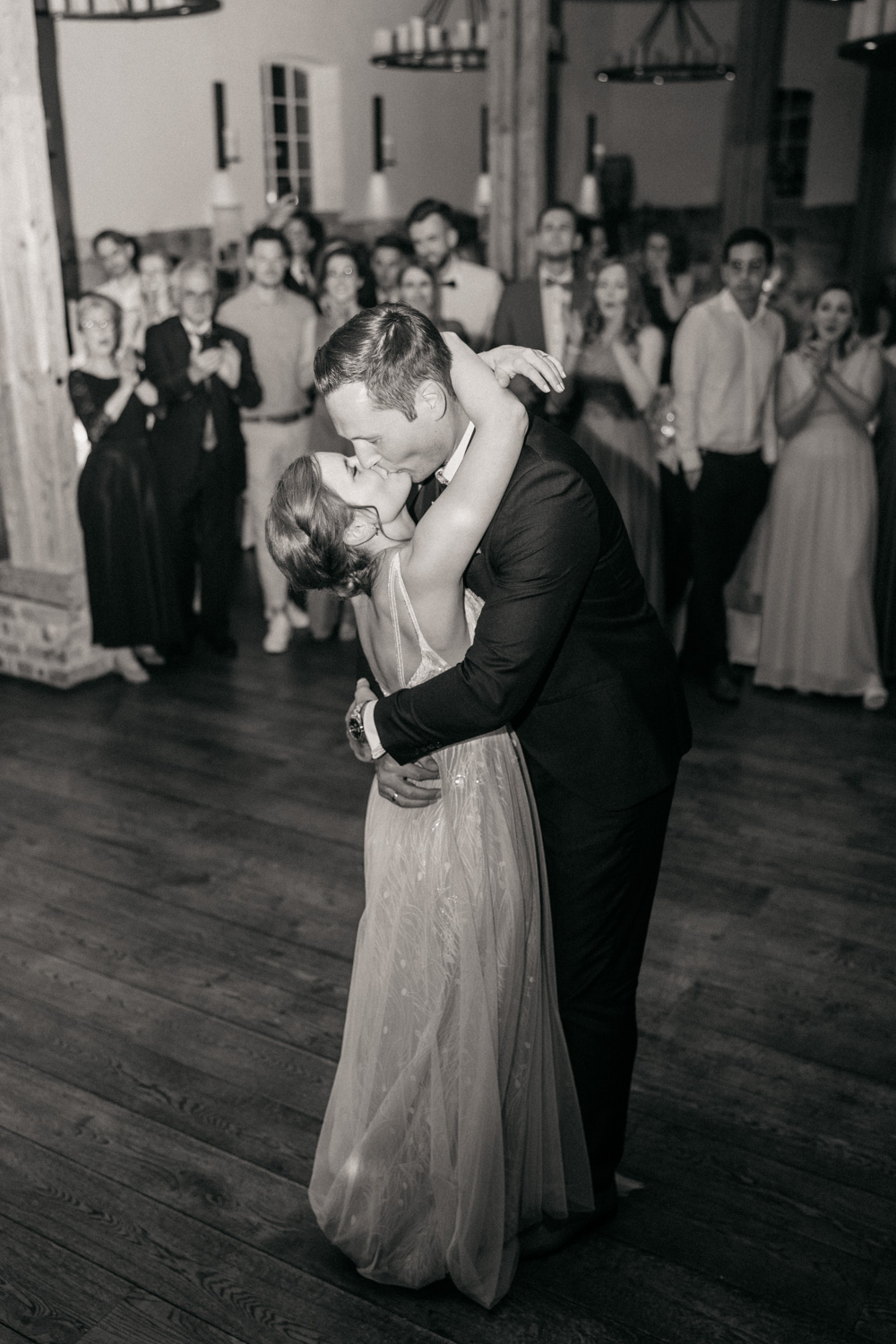Brautpaar während ihres Hochzeitstanzes. Küssen sich und die Gäste jubeln im Hintergrund.