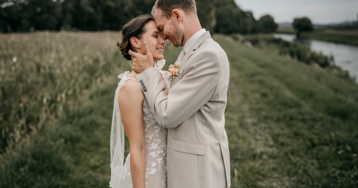 A bride and a groom. He is grabbing her face and is very close to her. Both smiling.